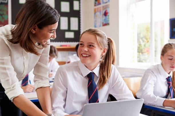 Teacher helping a UK school student at a laptop, GCSE and A-level classroom
