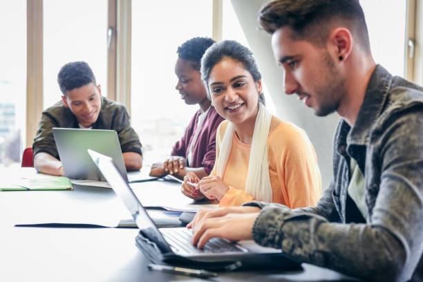 UK university students working together on laptops around a table for group coursework