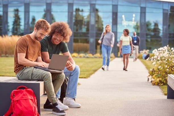 Two UK university students reviewing essay feedback together on a laptop outside on a campus bench