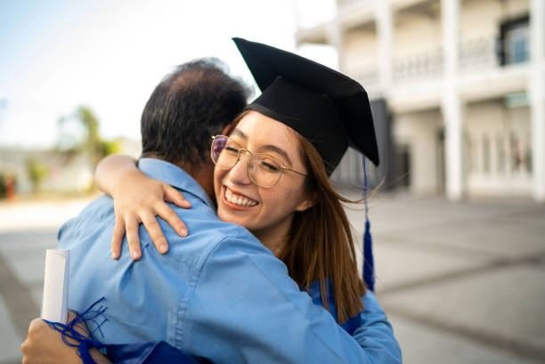 UK graduate hugging a parent, holding her diploma, both smiling