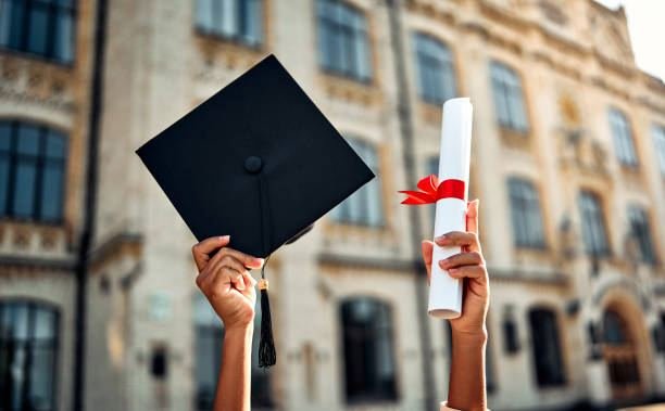 Graduates raising a cap and diploma tied with a red ribbon outside a university building