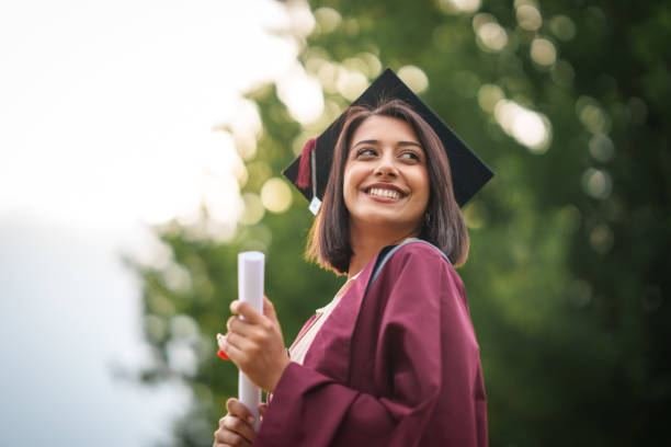 Smiling Masters graduate in a maroon gown and cap holding a diploma