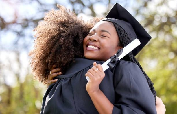 Two UK graduates hugging and smiling in caps and gowns